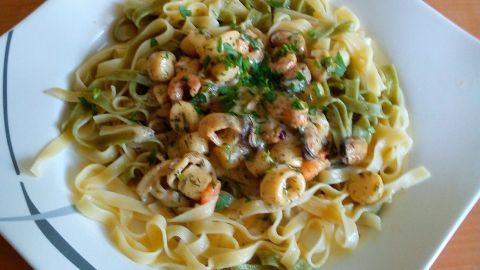 Pasta mit frischen Meeresfrüchten in Kräuterrahm, garniert mit Kräutern, serviert auf einem modernen Teller.