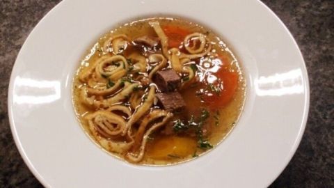 Eine Schüssel Rindsuppe mit zarten Fleischstücken und Gemüse schwimmt in aromatischer Brühe auf einem dunklen Tisch.