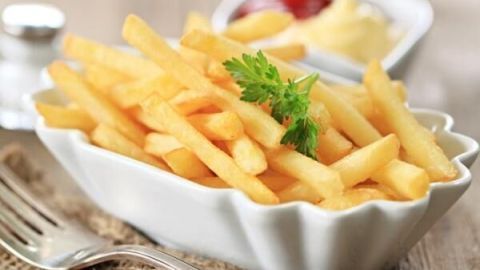 Pommes frites in einer weißen Schale, verziert mit Petersilie, auf einem Holztisch. Im Hintergrund Ketchup und Mayonnaise.