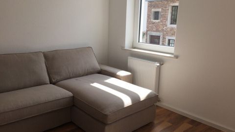 Ein helles, gemütliches Wohnzimmer mit einem grauen Ikea-Sofa, das in Sonnenlicht getaucht ist, bietet eine einladende Atmosphäre.