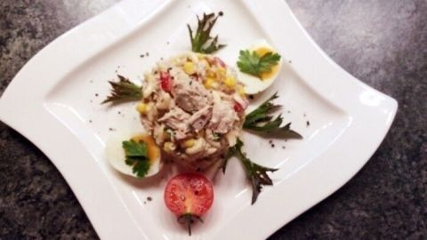 Ein ansprechend angerichteter Nudelsalat mit Thunfisch, garniert mit frischen Kräutern und Tomatenscheiben, liegt auf einem eleganten Teller.