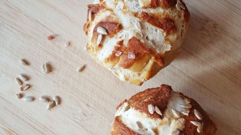 Zwei goldbraune Laugenbrötchen liegen auf einem Holzbrett, umgeben von einigen verstreuten Sonnenblumenkernen.