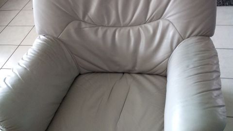 Ein beiger Ledersessel steht in einem modernen Wohnzimmer. Er sieht gebraucht aus und benötigt Pflege und Reinigung.