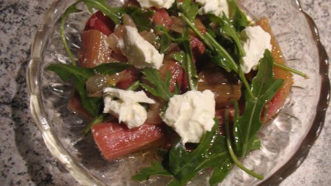 Ein frischer Salat aus Rhabarber und Rucola wird mit Frischkäse garniert und auf einem gläsernen Teller serviert.