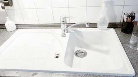 Eine weiße Granitspüle steht auf einer Arbeitsplatte, während ein Wasserhahn über ihr schwenkt und die Wand gefliest ist.