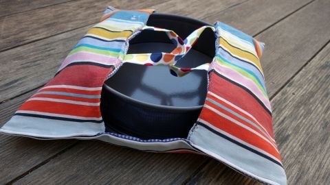 Eine bunte Kuchentasche aus Geschirrtüchern liegt auf einem Tisch und hält ein schwarzes Backutensil.