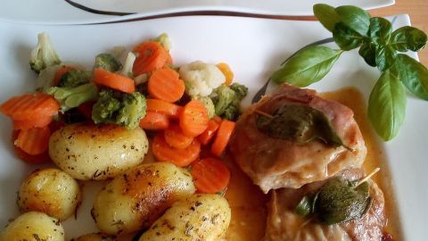 Zwei Teller mit Saltimbocca alla Romana, umgeben von Kartoffeln und buntem Gemüse, serviert auf einem Holztisch.