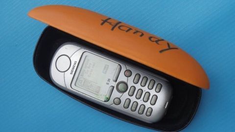 Ein Handy liegt in einem schwarzen Etui mit orangem Deckel, das offen ist. Das Handy scheint einsam auf dem Boden zu liegen.