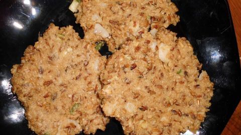 Haferpuffer aus ganzen Haferkörnern liegen auf einem schwarzen Teller, golden gebraten und appetitlich angerichtet.