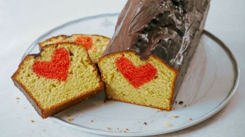 Der saftige Rührkuchen mit Herzen wird auf einem Teller präsentiert, mit einer Schokoladenglasur und roten Herzmuster im Inneren.