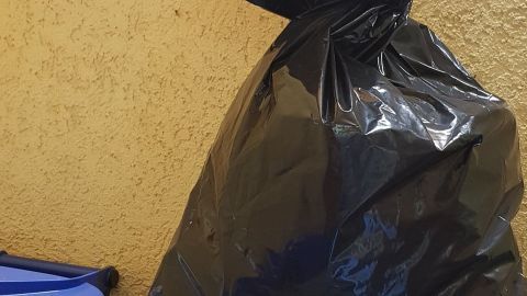 Schwarze Mülltüte steht auf einem Container, um die Abfälle von Tieren fernzuhalten, in einem urbanen Umfeld.