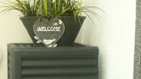 Eine platzsparende Auflagenbox steht an der Wand, dekoriert mit einem Blumenkübel, ideal für Terrasse oder Balkon.