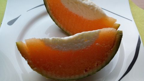 Zwei halbe Melonenstücke liegen auf einem weißen Teller. Die orangefarbene Frucht hat einen cremigen Joghurtkern.