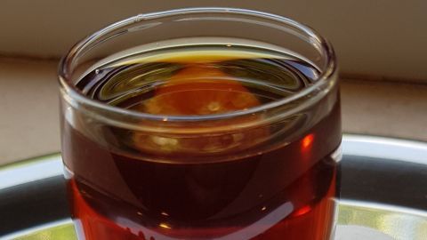Ein Glas Kaffeelikör steht auf einem Tablett, umgeben von Kaffeebohnen, bei hellem Tageslicht auf einem Tisch.