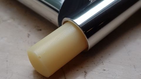 Ein silberner Lippenbalsam-Stift liegt geöffnet auf einer hellen Oberfläche, der Balsam ist teilweise herausgedrückt.
