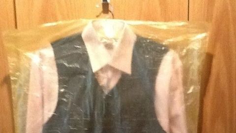 Kleidung wie z. B. Anzug oder Sakko mit einem Gelben Sack oder durchsichtiger Plastiktüte staubfrei im Schrank verstauen. Ein graues Sakkо und ein rosa Hemd sind in einer durchsichtigen Schutzhülle staubfrei aufbewahrt, aufgehängt an einem Haken.