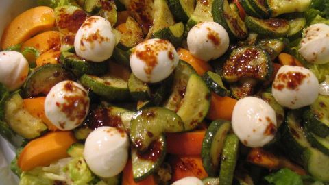 Ein bunter Salatteller präsentiert frische Zutaten, während Mozzarellakugeln auf knackigem Gemüse und Salat liegen.