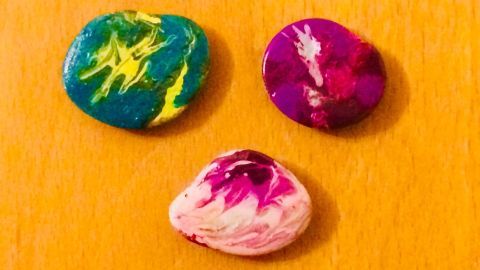 Bunte Marmorierte Steine liegen auf einer Holzoberfläche und präsentieren eine kreative Gestaltung für ein Gastgeschenk.