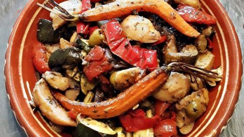 Ein bunter mediterraner Ofengemüse-Kartoffelsalat liegt auf einem rustikalen Teller und wird appetitlich präsentiert.