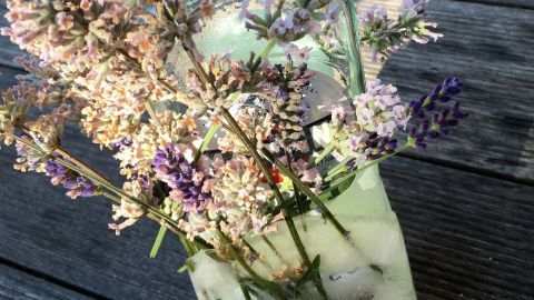 Ein Flaschenkühler aus Eis umgibt eine Flasche, die mit bunten Blumen dekoriert ist, auf einer Holzoberfläche.