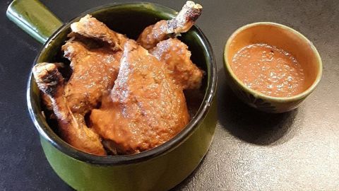 Zartes Hähnchen liegt in einer grünen Schüssel, neben einer kleinen Schale mit Sauce in einem dunklen Umfeld.