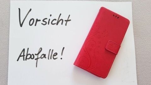 Ein rotes Smartphone-Cover liegt neben einer Warnung vor Abofallen auf einem weißen Blatt, das zur Vorsicht mahnt.