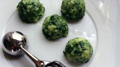 Auf einem weißen Teller liegen fünf grüne Kartoffelpüree-Kugeln, daneben ein Kugelausstecher für eine hübsche Anrichtung.