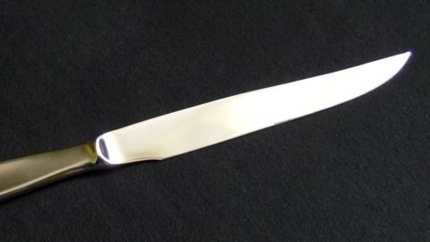 Ein glänzendes Edelstahlmesser liegt auf schwarzem Stoff, bereit zum Schneiden in einer eleganten Küchenumgebung.