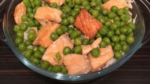Saftiger Lachs liegt auf Reis, umgeben von frischen grünen Erbsen, alle in Zitronenbutter angerichtet auf einem Tisch.