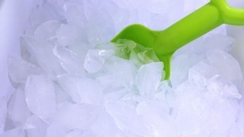 Eiswürfel liegen in einem Behälter, während ein grüner Schaufel das Eis umschichtet, um Lebensmittel kühl zu halten.