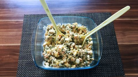Ein farbenfroher russischer Oliviersalat mit Hähnchen in einer Glasschale, serviert auf einem Holztisch, umrundet von Besteck.