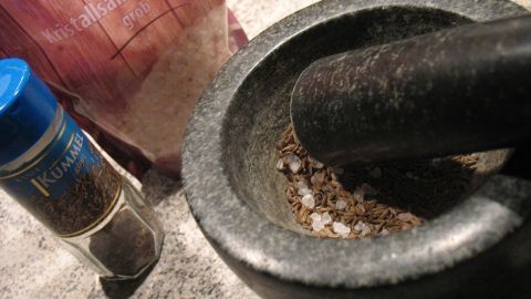 Ein Mörser zermahlt Kümmel in einer Küche, um den Geschmack zu verstärken, während eine Gewürzdose daneben steht.