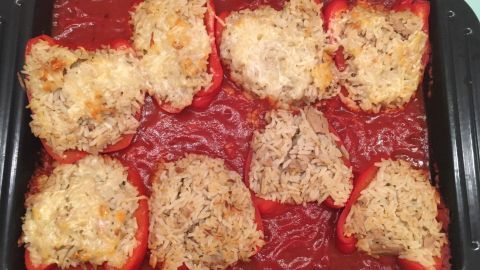Gefüllte Paprikaschoten liegen in einer goldbraun überbackenen Schicht, umgeben von roter Tomatensoße in einer Auflaufform.