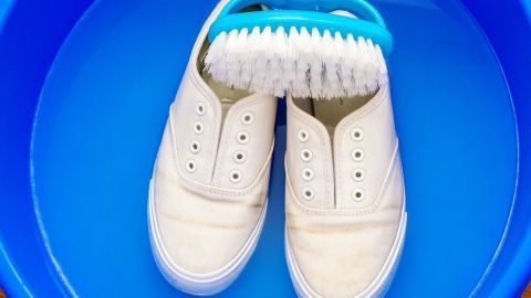 Weiße Sneaker liegen in einem blauen Behälter, während eine Bürste zum Reinigen bereitliegt, um Gelbe Ränder zu entfernen.