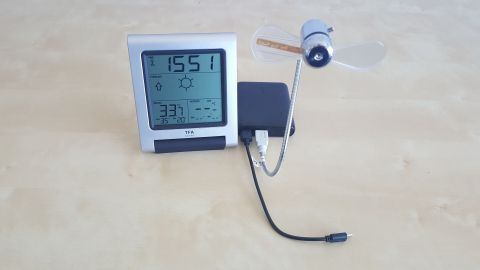 Ein Thermometer mit digitaler Anzeige misst die Temperatur und Luftfeuchtigkeit, während ein kleiner Ventilator kühlt.