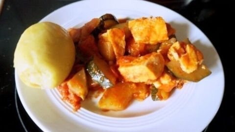 Eine Zucchini-Pfanne mit Lachs auf einem weißen Teller, umgeben von gekochten Kartoffeln, steht appetitlich auf dem Tisch.
