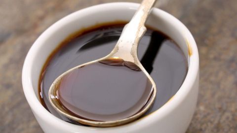 Ein kleiner weißer Schüsselchen mit dunkler Flüssigkeit, auf einem Holzuntergrund, hält einen Löffel für die Anwendung bei Hautproblemen.