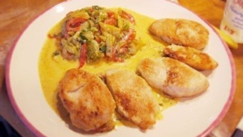 Ein Teller mit gebratenem Paprikagemüse und zarten Filets, angerichtet auf einer Holzoberfläche.