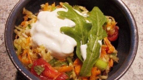 Ein bunter Mairübchen-Karotten-Salat mit frischen Tomaten, Rucola und einem Klecks Joghurt in einer Schüssel.