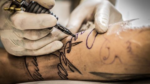 Ein Tätowierer arbeitet konzentriert an einem Arm, während er präzise Linien für das erste Tattoo zeichnet.