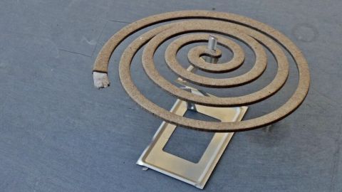 Eine spiralförmige Mücken-Spirale ruht auf einem metallischen Halter und wirkt als natürlicher Insektenschutz im Freien.