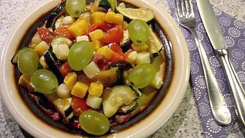 Bunte Zucchini-Paprika-Käse-Salat-Mischung in einer Schüssel, umgeben von Besteck auf einem gemusterten Tisch.