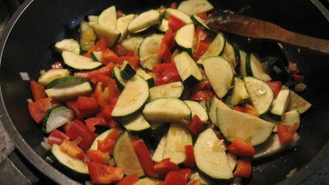Gemischte Zucchini- und Paprikastücke werden in einer Pfanne gebraten, um einen schmackhaften Käse-Salat zuzubereiten.