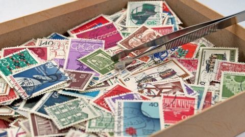 Eine Schachtel voller bunter Briefmarken wird mit einer Pinzette durchsucht – Leidenschaft und Geldanlage liegen nah beieinander.