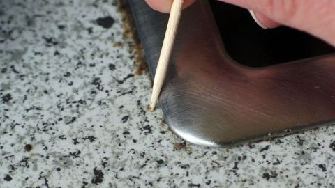 Eine Hand hält einen Zahnstocher und reinigt die Kante unter einem Glaskeramikfeld in einer modernen Küche.