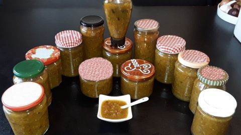 Einige Gläser mit Gurkenrelish stehen in einer ansprechenden Anordnung auf einem Tisch, während ein Löffel mit dem Aufstrich danebenliegt.
