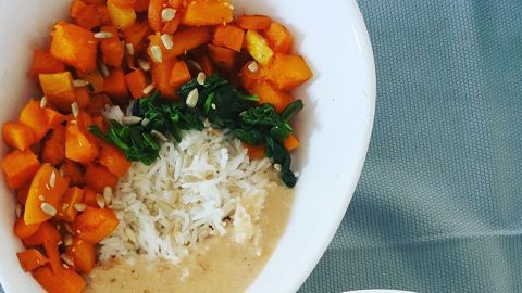 Veganes Kürbis Süßkartoffel Curry liegt in zwei Schalen, umgeben von Reis und Erdnusssauce, appetitlich angerichtet.