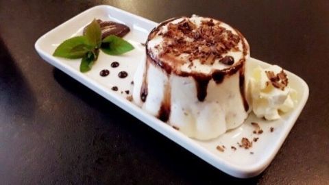 Ein Joghurteis voller Frische, dekoren mit Schokoladensauce, Sahne und Minzblättern, serviert auf einem weißen Teller.