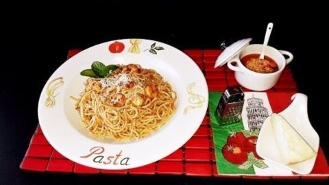 Pasta wird auf einem dekorativen Teller serviert, umgeben von frischen Kräutern und einer Sauce in einem kleinen Topf.