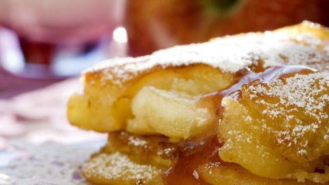 Feine Apfelküchlein liegen appetitlich angerichtet, staubzuckerbestäubt und umgeben von einem unscharfen, rustikalen Ambiente.